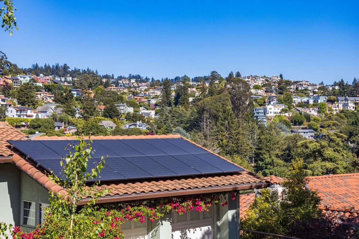 Solar panels on a residential rooftop with a hillside neighbourhood in the background